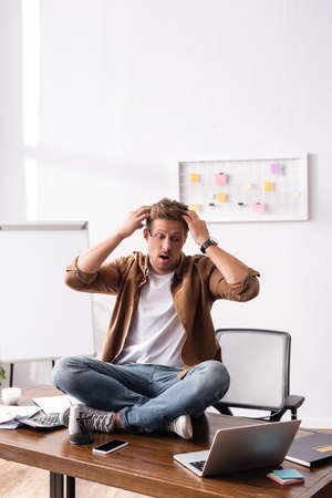 Shocked businessman looking at laptop while sitting on office tableの写真素材