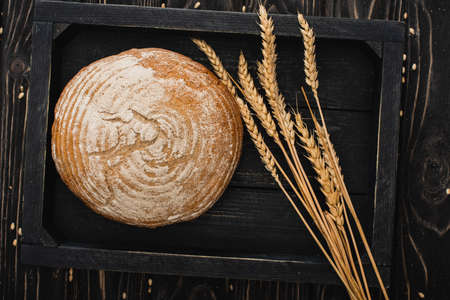 top view of fresh baked white bread loaf with spikelets on wooden black board