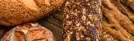 close up view of fresh baked bread loaves with spikelets on wooden surface, panoramic shot