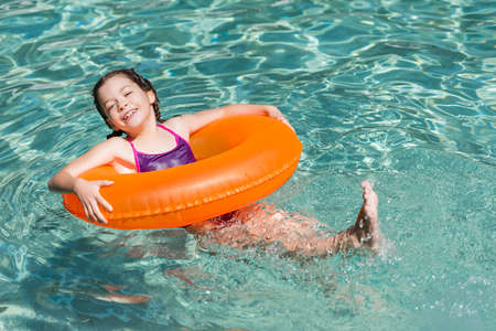 pleased girl looking at camera while swimming in pool on inflatable ring