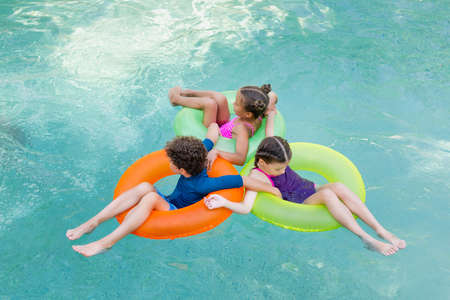 high angle view of boy and two girls floating in pool on colorful swim rings