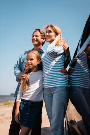 Selective focus of man hugging wife and daughter near car on beach