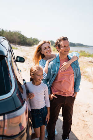Selective focus of woman embracing husband near daughter and auto on beach