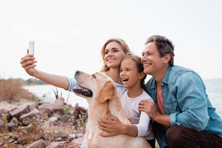 Selective focus of family taking selfie near golden retriever on beach