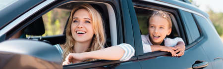 Panoramic shot of excited woman looking away while traveling with daughter in car