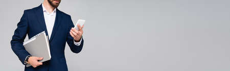 cropped view of businessman in blue blazer holding smartphone and folder isolated on gray, panoramic shotの写真素材