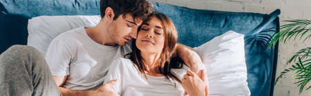 Panoramic concept of man hugging girlfriend in pajamas on bed