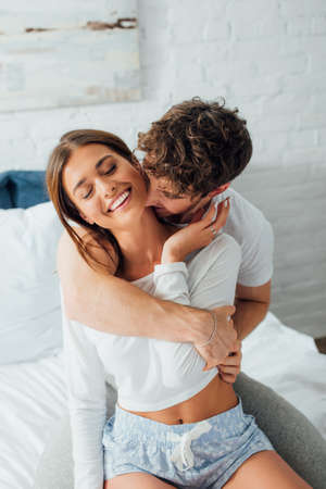 Man kissing in neck girlfriend in pajamas in bedroom