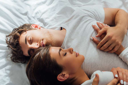Top view of young couple embracing with closed eyes on bedの写真素材