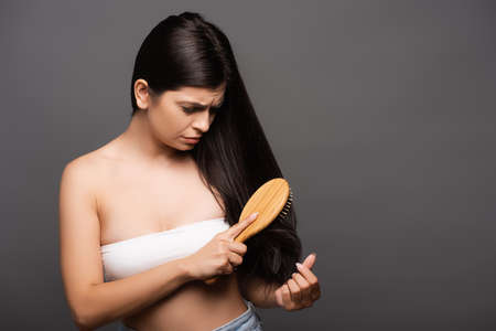 worried brunette woman brushing hair isolated on blackの写真素材
