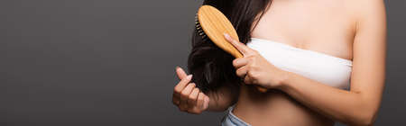 cropped view of brunette woman brushing hair isolated on black, panoramic shotの写真素材