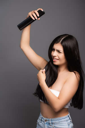 brunette long haired woman applying hair spray with closed eyes isolated on blackの写真素材