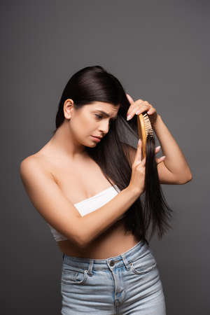sad brunette woman brushing hair isolated on blackの写真素材