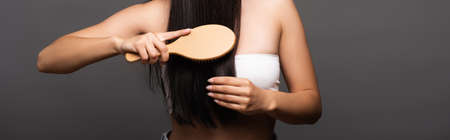 cropped view of brunette woman brushing shiny hair isolated on black, panoramic shot