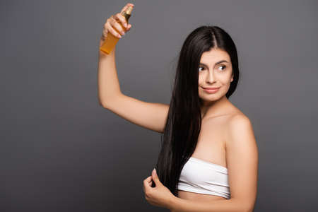 brunette woman spraying oil on hair isolated on blackの写真素材