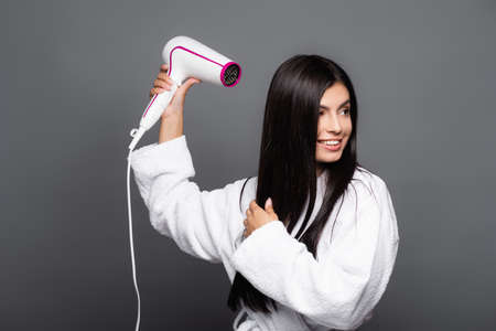 brunette long haired woman in bathrobe using hairdryer isolated on blackの写真素材