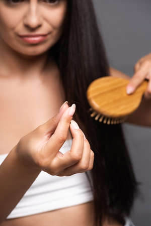 selective focus of brunette woman holding lost hair while brushing isolated on blackの写真素材