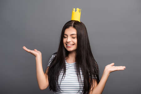 brunette long haired woman in paper crown with closed eyes smiling isolated on blackの写真素材