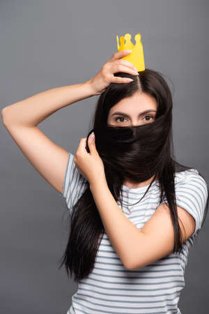 brunette woman in paper crown covering face with hair isolated on blackの写真素材