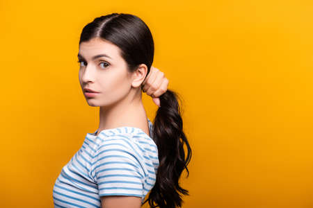 side view of brunette woman with curls holding hair isolated on yellowの写真素材