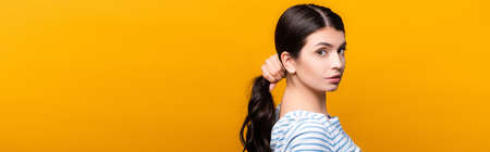 side view of brunette woman with curls holding hair isolated on yellow, panoramic shot