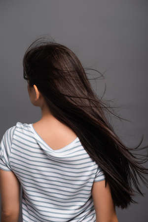 back view of wind blowing through hair of brunette woman isolated on blackの写真素材