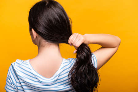 back view of brunette woman with curls holding hair isolated on yellowの写真素材
