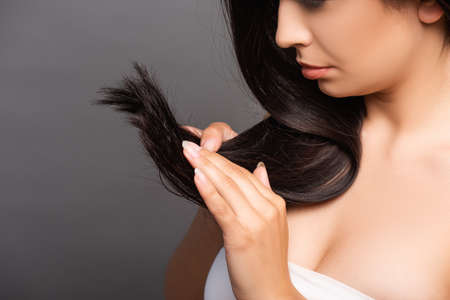 cropped view of upset brunette woman touching hair isolated on black