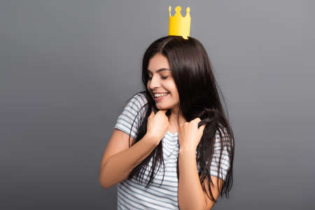 brunette long haired woman in paper crown with closed eyes smiling isolated on black