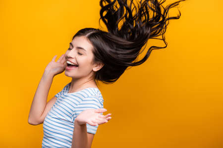 brunette long haired woman with curls jumping isolated on yellowの写真素材