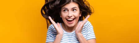 brunette long haired woman with curls jumping and smiling isolated on yellow, panoramic shotの写真素材