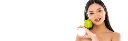 panoramic concept of young asian woman holding cosmetic cream and green apple near face isolated on whiteの写真素材