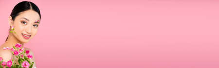 horizontal concept of asian woman with buds and petals on face and shoulder, holding tiny roses isolated on pinkの写真素材