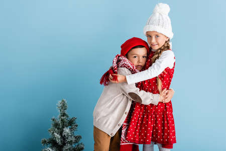 kids in winter outfit hugging near christmas tree on blueの写真素材