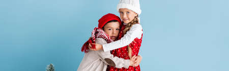 panoramic crop of kids in winter outfit hugging near christmas tree on blueの写真素材