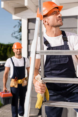 Selective focus of builder in hardhat standing on ladder near colleague and buildingの写真素材