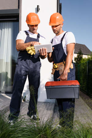 Selective focus of builders with tool belt and toolbox using digital tablet on urban street