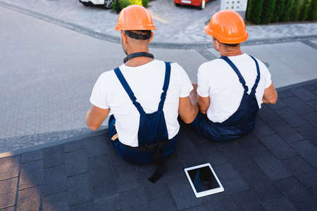 Back view of builders sitting near digital tablet on roof of building