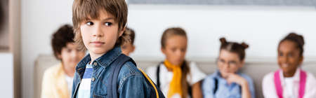 Panoramic image of schoolboy with backpack standing near multiethnic classmates in schoolの写真素材