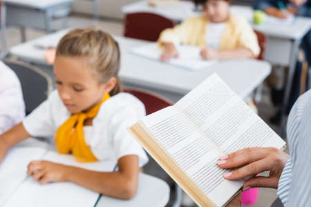 cropped view of teacher reading book near pupils in classroomの写真素材