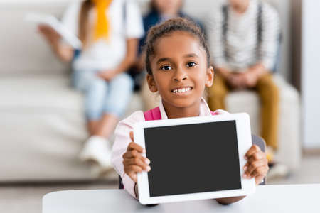 Selective focus of african american schoolgirl showing digital tablet with blank screen at desk
