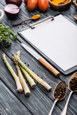 selective focus of blank clipboard near knife and vegetables on wooden surfaceの写真素材
