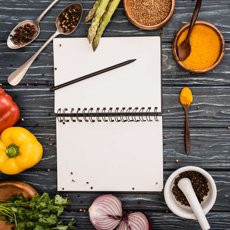 top view of fresh colorful vegetables and spices near blank notebook on wooden surfaceの写真素材