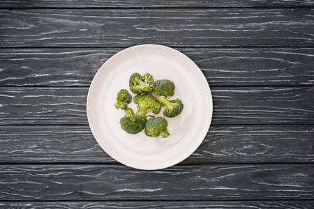 top view of fresh broccoli on plate on wooden surface