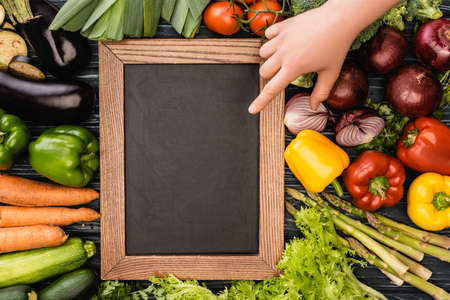 cropped view of person pointing at empty chalkboard near fresh colorful vegetablesの写真素材