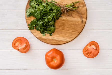 top view of parsley on chopping board near tomatoes on white wooden tableの写真素材