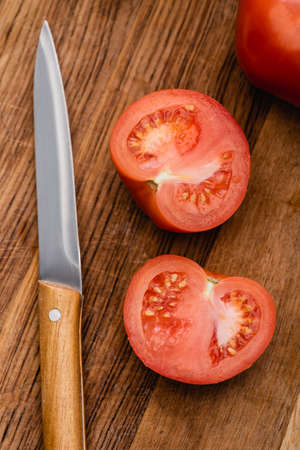 top view of ripe tomato halves on wooden chopping board with knifeの写真素材