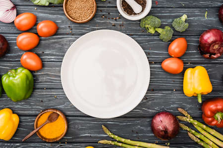 top view of fresh colorful vegetables and spices near empty plate on wooden surfaceの写真素材