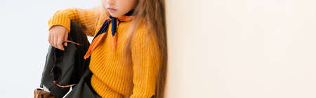 cropped view of fashionable blonde girl in autumn outfit with sunglasses on beige and white...