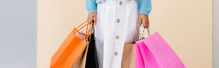 cropped view of girl in white skirt and blue sweater with colorful shopping bags near beige wall, panoramic shotの写真素材